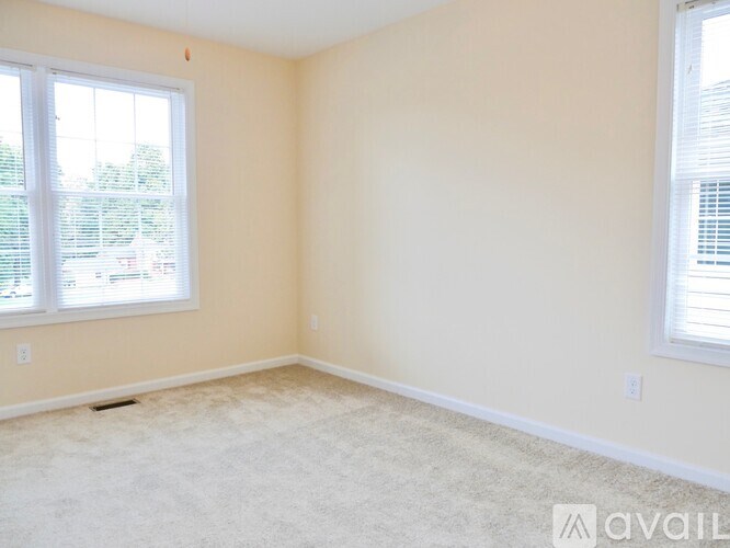 A room with a carpeted floor and two windows.