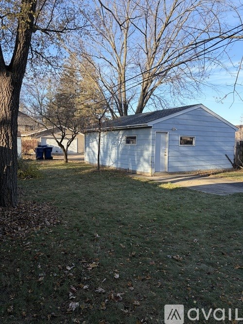 A white shed sits in a grassy yard with trees in the background.