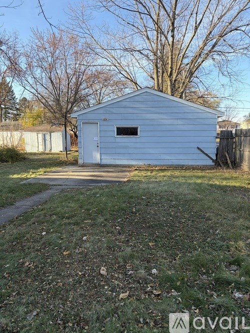 A small white shed sits in a grassy area with a pathway leading to it.
