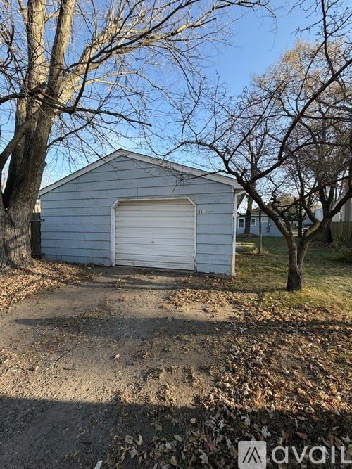 A grey garage with a white door is surrounded by trees and grass.