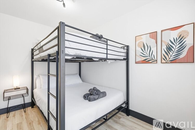 A bunk bed with a white mattress and a grey blanket is in a room with two framed artworks on the wall.