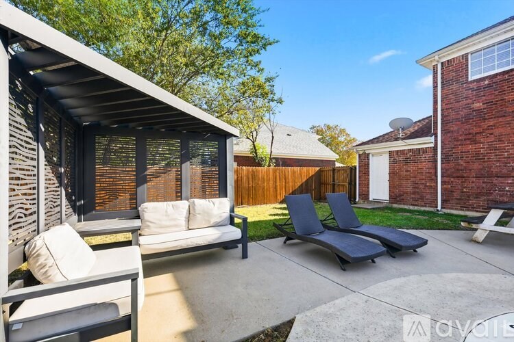 A sunny backyard with a white couch and black lounge chairs.