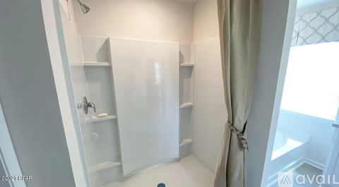 A small, white bathroom with a shower and a window.