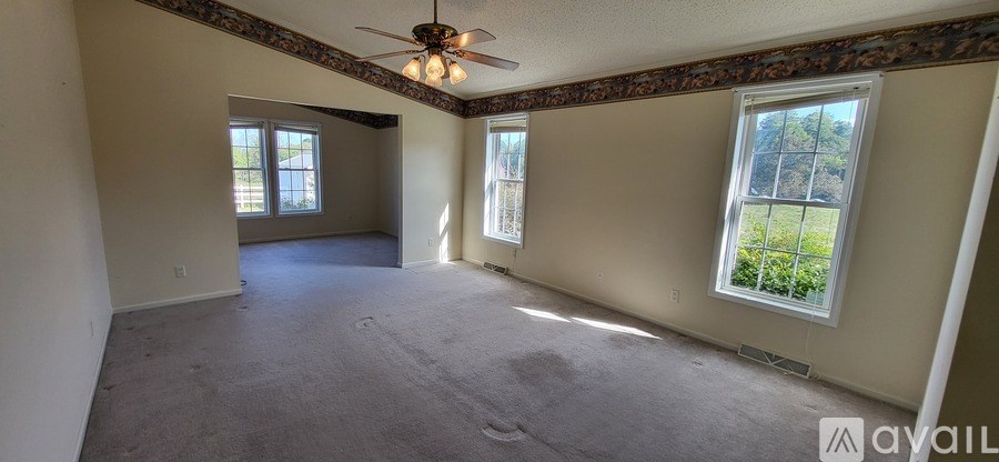 A spacious room with a ceiling fan and two windows.