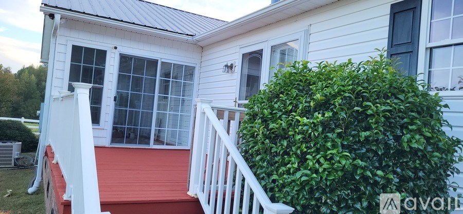 A white house with a red deck and a green bush.