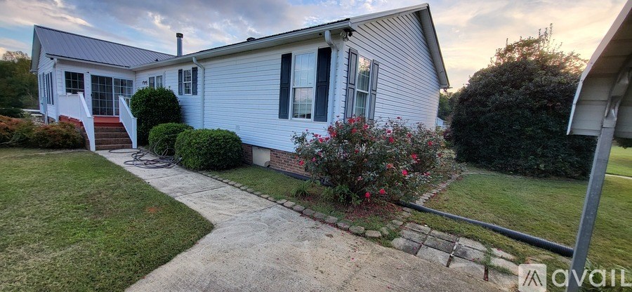A house with a white porch and a red flower bush in front.