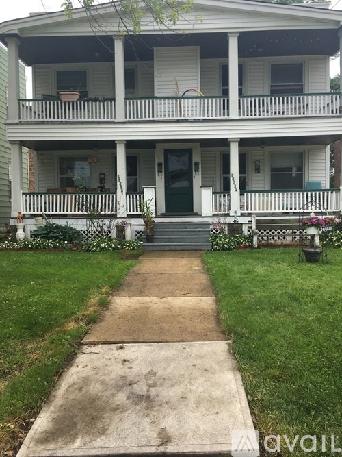 A white two story house with a green door and a concrete walkway leading to it.