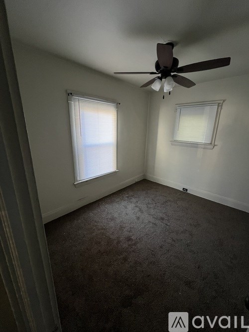 A room with a ceiling fan and two windows.