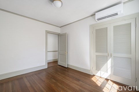 A room with wooden floors and white walls, with a closed door and an open door.
