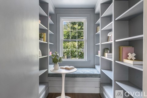 A small table with a vase of flowers on it sits in the corner of a room with shelves on the walls.