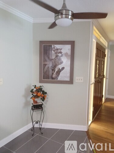 A room with a fan, a painting and a plant on a table.