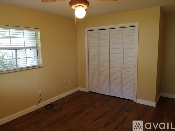 A room with a window, a fan, and a wooden floor.