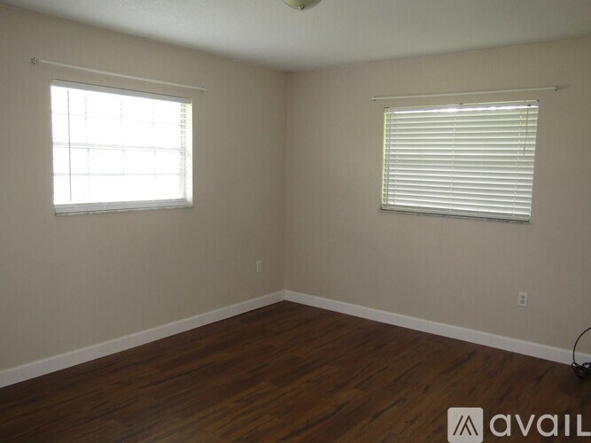 A room with wooden floors and two windows with blinds.