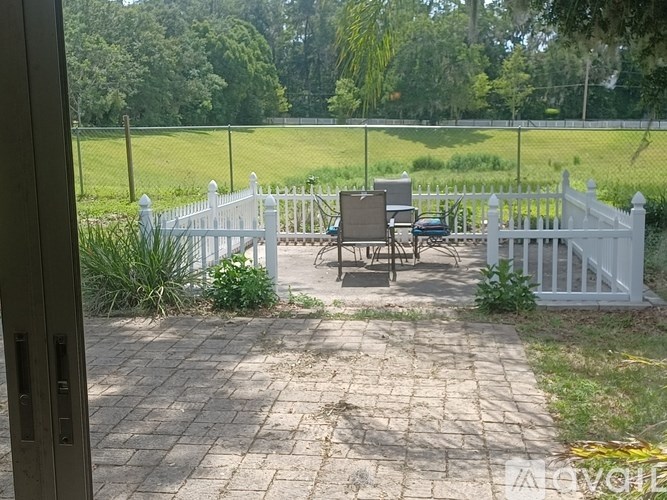 A white picket fence surrounds a patio with a table and chairs.