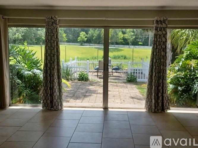 A view from a room looking out to a patio with a white fence and greenery.