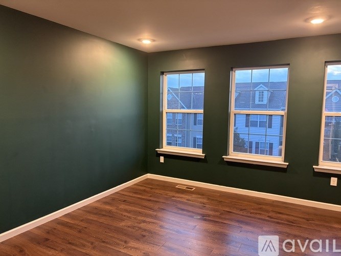 A room with dark green walls and wooden flooring with two windows.