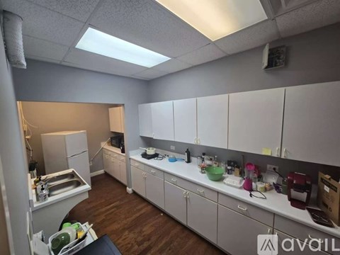 A clean and organized office kitchen with white cabinets and a variety of kitchen appliances.
