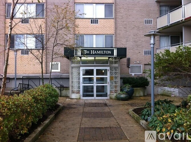The Hamilton building entrance is framed by bushes and trees.