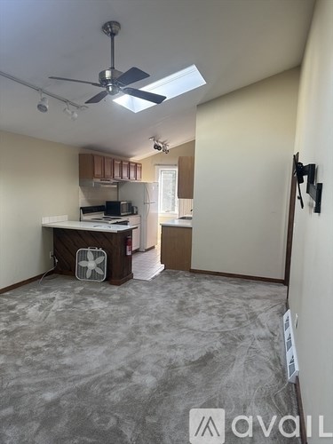 A room with a ceiling fan and a kitchen area in the background.