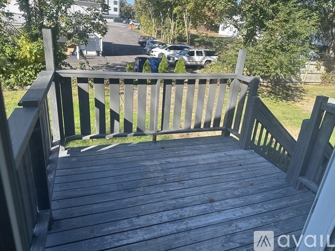 A wooden deck with a railing and a view of a parking lot and trees.
