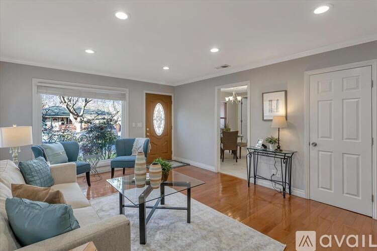 A well-lit living room with a glass coffee table and a view of the outdoors through a large window.