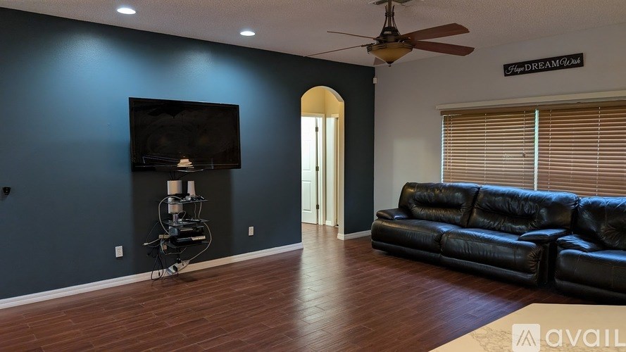 A living room with a black leather couch and a television mounted on the wall.