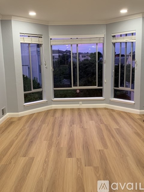 A room with wooden flooring and two windows.
