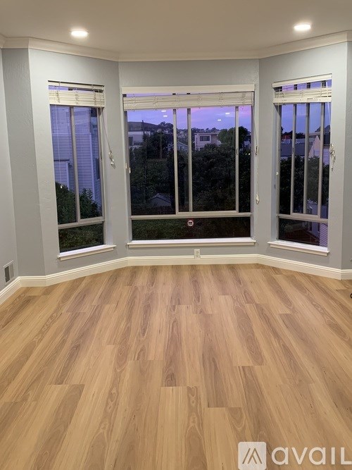 A room with wooden flooring and two windows.
