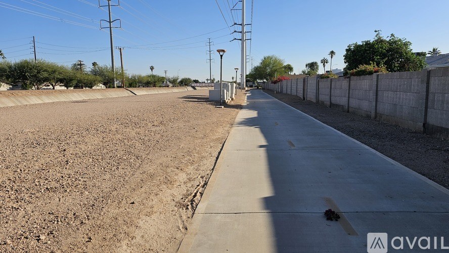 A long, empty sidewalk stretches into the distance with a wall on one side and a fence on the other.
