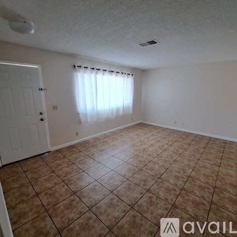 A room with brown tiled flooring and a window with white curtains.