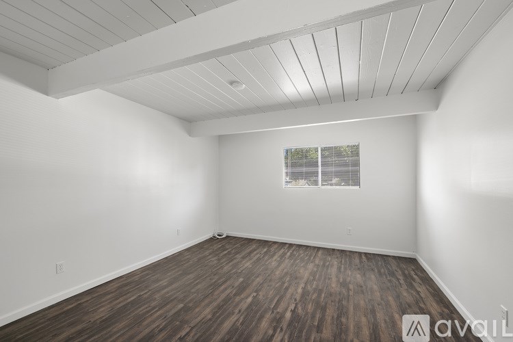 A spacious room with wooden flooring and a window with blinds.