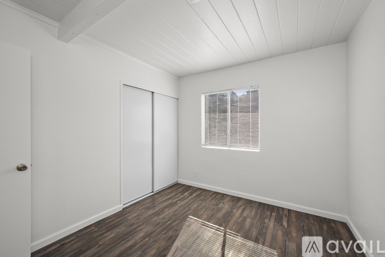 A room with a slanted ceiling, a window with blinds, and a wooden floor.