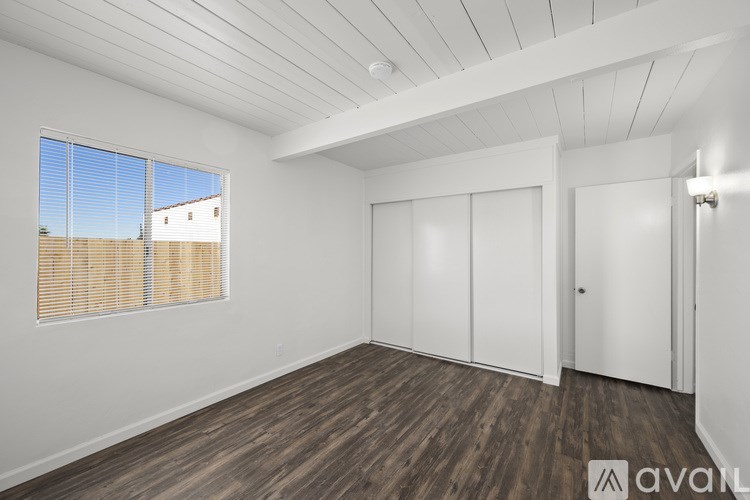 A room with wooden floors and white walls, with a window showing a view of a building outside.