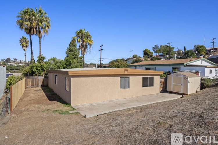A house with a brown roof and a brown fence is surrounded by palm trees.