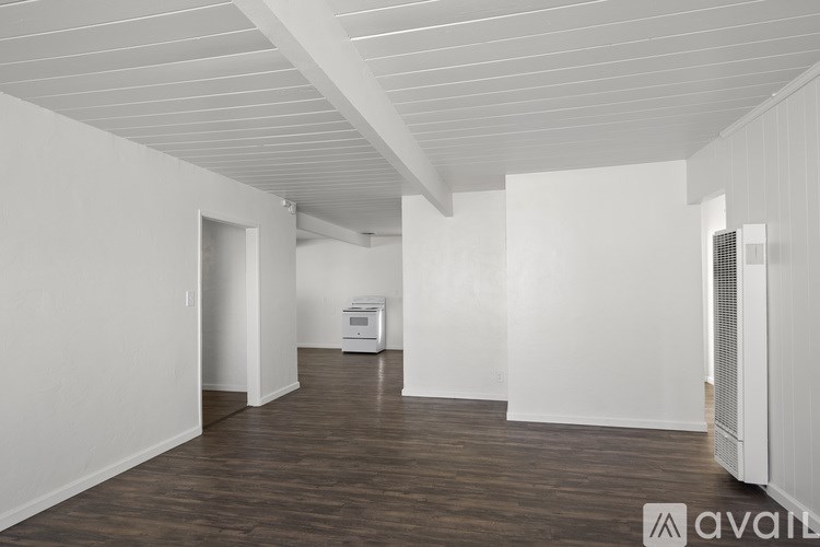 A spacious room with wooden flooring and white walls, featuring a white ceiling with exposed beams and a white air conditioning unit on the right wall.
