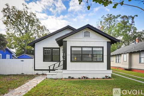 A small white house with a black door and windows is for sale.