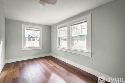 A room with two windows and a wooden floor.