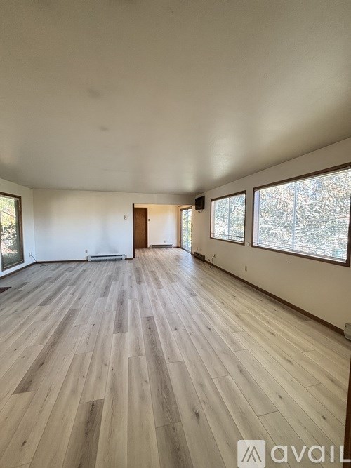 A spacious room with wooden flooring and large windows.