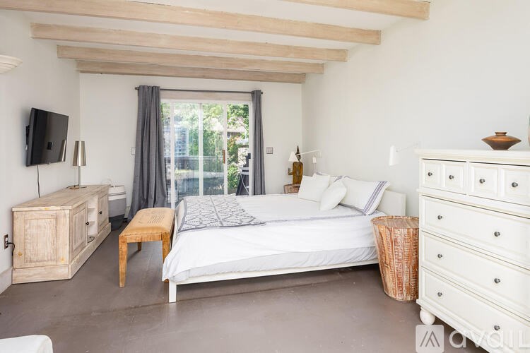 A bedroom with a large bed, a TV, and a window with curtains.
