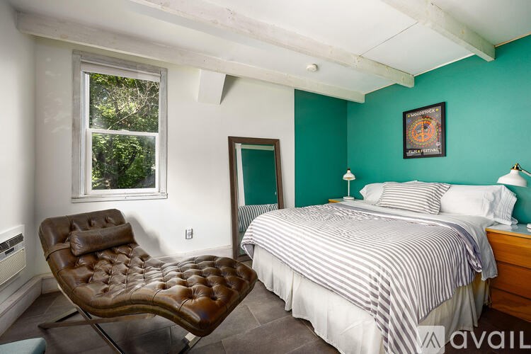 A bedroom with a bed, chair, and painting on the wall.