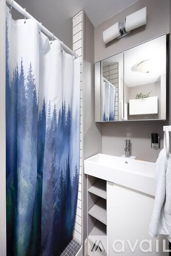 A bathroom with a white sink and a shower curtain with trees on it.