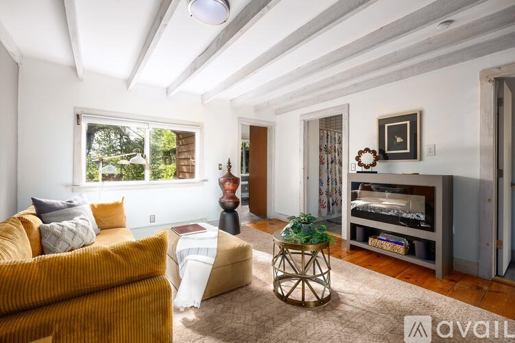 A living room with a yellow couch, a white ottoman, and a glass door leading to a balcony.