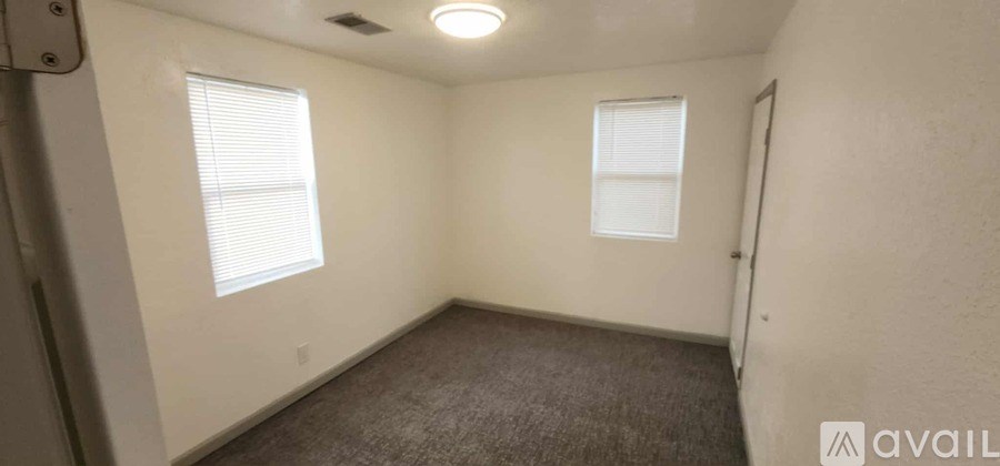 A small, empty room with two windows and a carpeted floor.