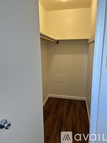 A white door with a silver handle is open to a small room with a wooden floor and white walls.