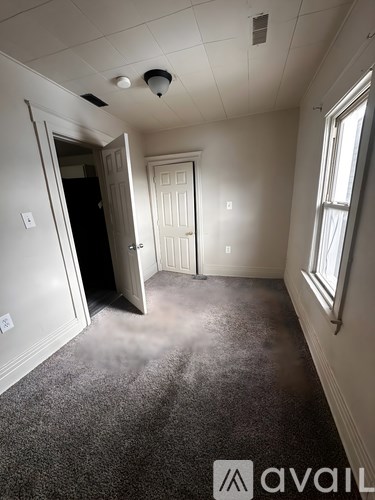 A room with a carpeted floor and a window on the right side.