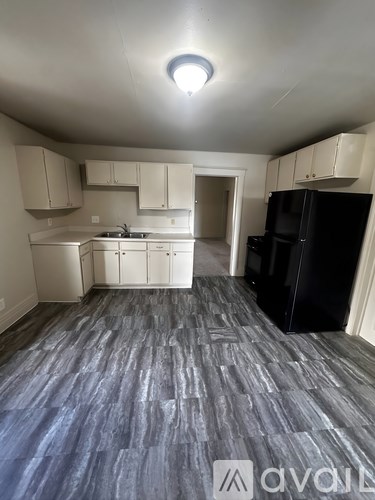 A kitchen with a black refrigerator and a wooden floor.
