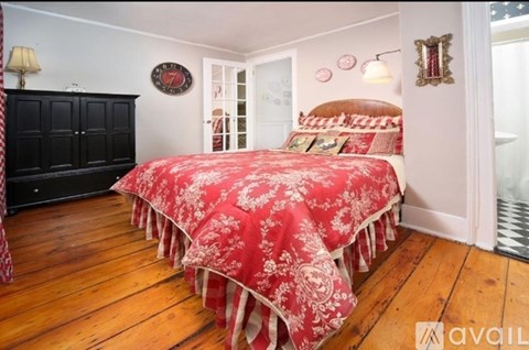A bedroom with a red bedspread and wooden floors.