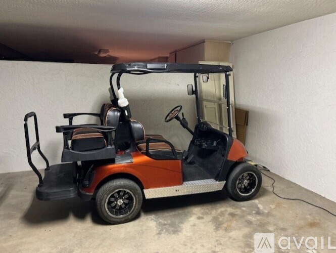 A small orange and black golf cart is parked in a garage.