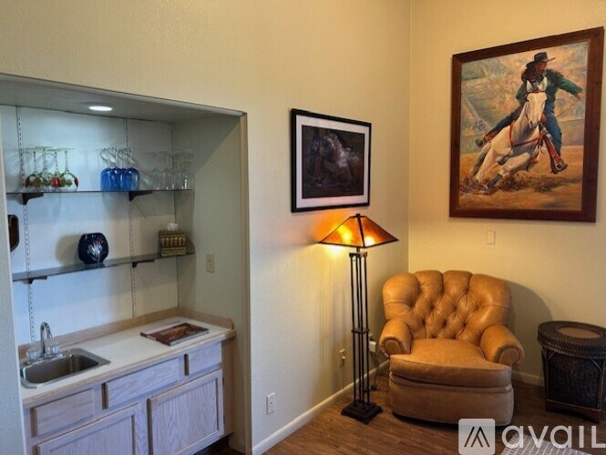 A room with a brown chair, a painting, and a lamp.