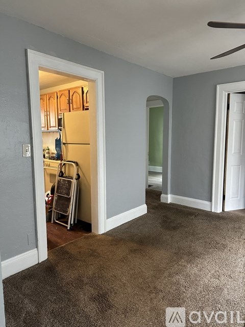 A room with a carpeted floor and a white door leading to a kitchen.